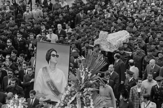 صورة بالأبيض والأسود لحشد هائل يحمل نعش أم كلثوم المغطى بالورود وصورة كبيرة مؤطرة لها عبر الشارع.